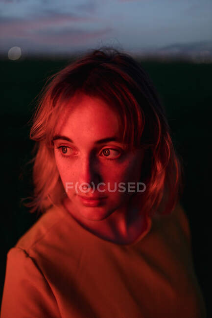 Мрійлива молода жінка в вінтажному стилі одягається, дивлячись в очі, стоячи на самоті в темному трав'яному полі проти хмарного сонцестояння в сутінках — стокове фото