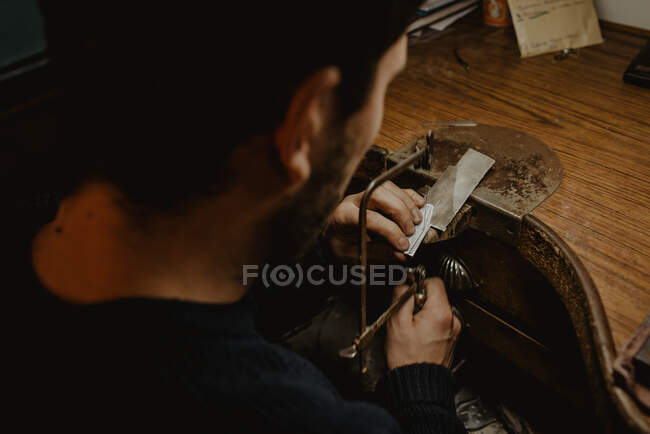 Goldsmith cutting metal with saw while making jewellery in workshop — Stock Photo