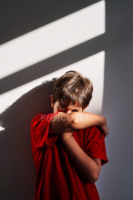 Irritado menino irreconhecível cobrindo rosto com as mãos e chorando enquanto estava perto da parede em casa — Fotografia de Stock