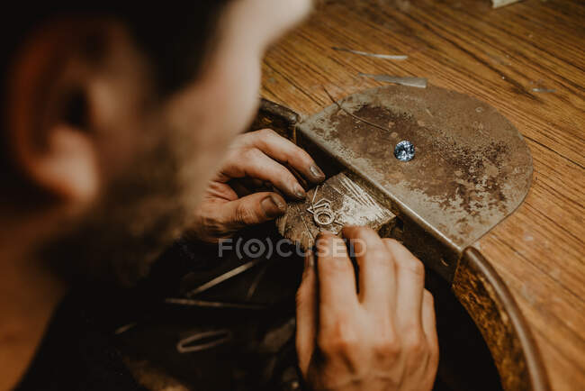 Bijoutier tenant la bague inachevée dans des mains sales et vérifiant la qualité dans l'atelier — Photo de stock