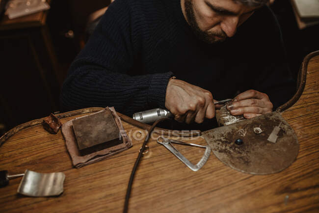 Joyero usando la máquina de pulir profesional en el banco de trabajo mientras que hace el anillo de metal en taller - foto de stock