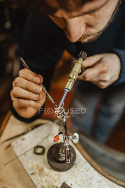 Анонімний золотошукач використовує паяльник для нагрівання крихітного металевого орнаменту при виготовленні ювелірних виробів на верстаті — стокове фото