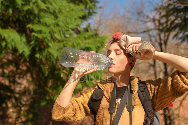 Thirsty female traveler with backpack enjoying fresh water on sunny day in nature — Stock Photo