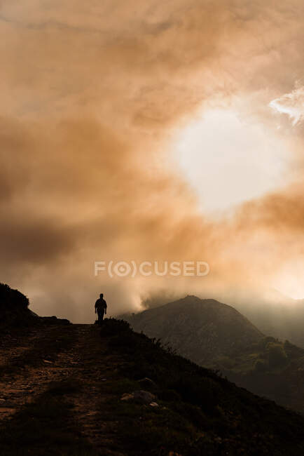 Silhouette d'explorateur anonyme lointain admirant le terrain montagneux contre le ciel nuageux levant le matin dans la nature — Photo de stock
