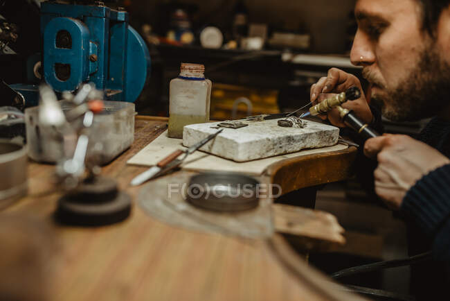 Goldsmith using blowtorch to heat tiny metal ornament while making jewellery on workbench — Stock Photo