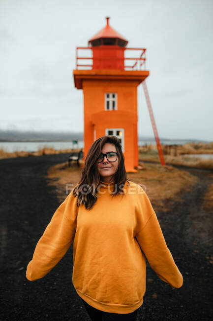 Mulher feliz de pé perto do farol laranja perto do mar — Fotografia de Stock