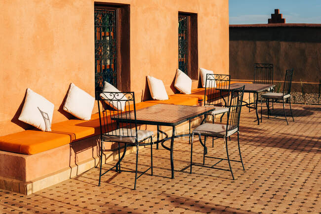 Almohadas suaves a lo largo de la pared de piedra con sillas y mesas al aire libre cómoda terraza de café en Marruecos - foto de stock