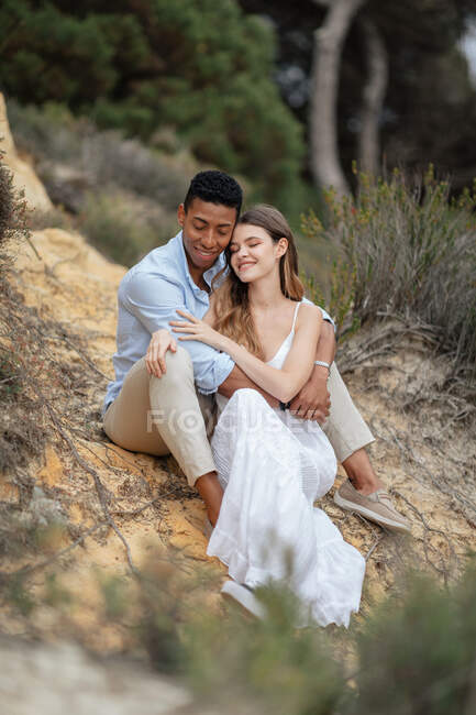Вміст багаторасової пари молодят, що сидять в лісі і обіймаються в день весілля — стокове фото