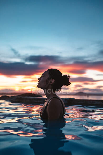 Вид сбоку на молодую женщину в купальнике, позирующую в голубой воде между скалами — стоковое фото