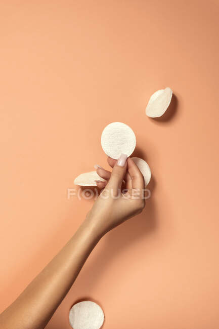 Crop unrecognizable woman with manicure and delicate skin demonstrating clean cotton pad on beige background — Stock Photo