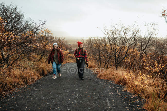 Jovens turistas felizes no inverno desgaste indo na estrada da floresta e céu nublado — Fotografia de Stock