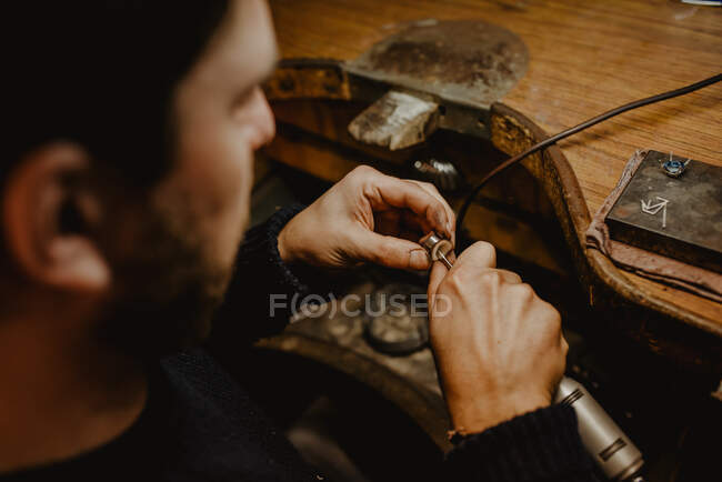 Unrecognizable jeweler using professional polishing machine on workbench while making metal ring in workshop — Stock Photo