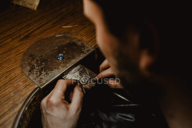 Gioielliere che tiene anello incompiuto in mani sporche e controlla la qualità in officina — Foto stock