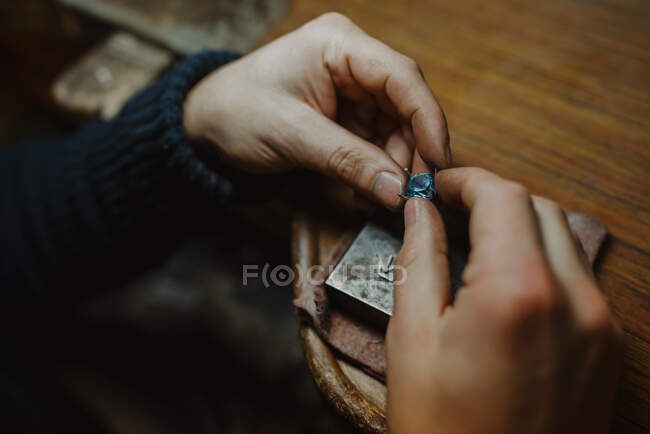 Irreconocible orfebre sosteniendo gema y adorno de metal sobre la mesa mientras hace el anillo en el taller - foto de stock