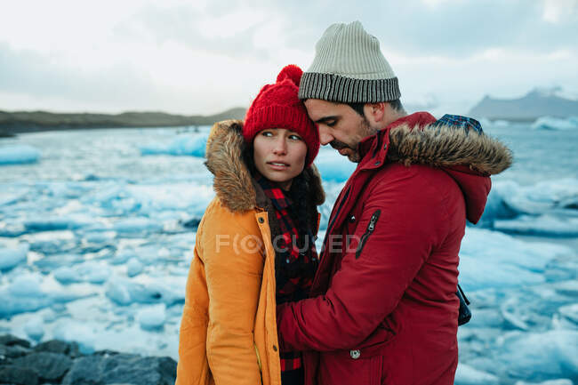 Vista lateral do homem e da mulher novos no desgaste do inverno com câmeras profissionais que estão na costa perto da água com gelo — Fotografia de Stock