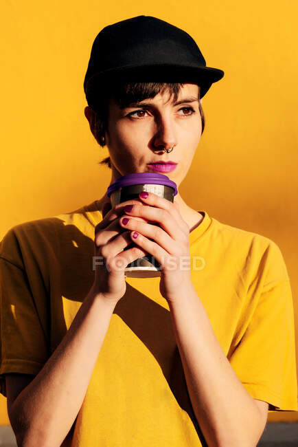 Молода неформальна жінка в модній кепці, що виносить гарячий напій на жовтий фон — стокове фото