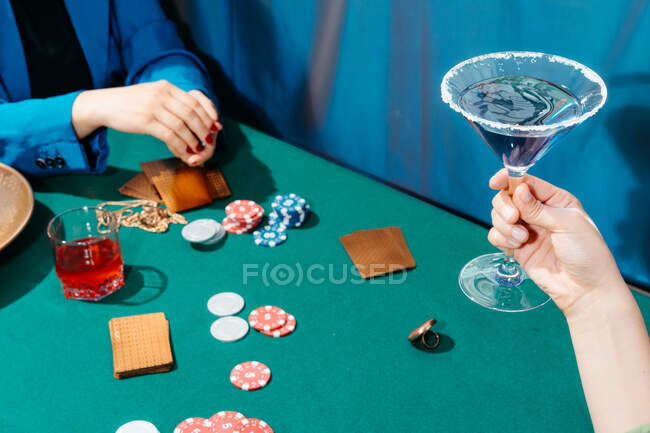Cortar amigos femininos irreconhecíveis sentados à mesa verde com cartões e fichas de poker enquanto joga — Fotografia de Stock