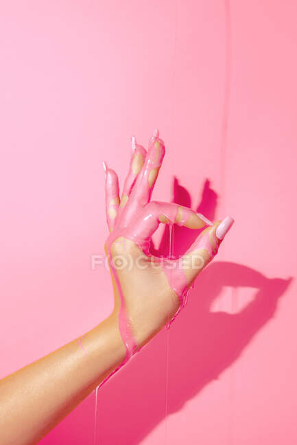 Crop unrecognizable woman showing hand with manicure and bright paint fluids on pink background — Stock Photo