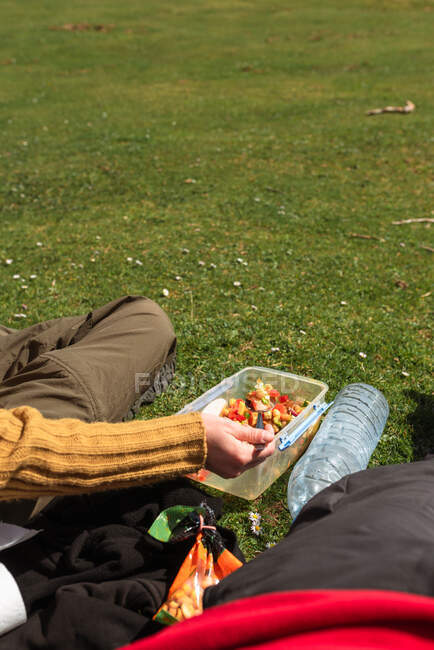Irriconoscibile viaggiatore delle colture seduto sul prato e che pranza durante l'avventura estiva nella giornata di sole — Foto stock