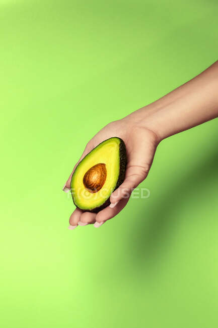 Ernte unkenntlich weiblich zeigt köstliche geschnitten reife Avocado mit weichem Fruchtfleisch auf leuchtend grünem Hintergrund — Stockfoto