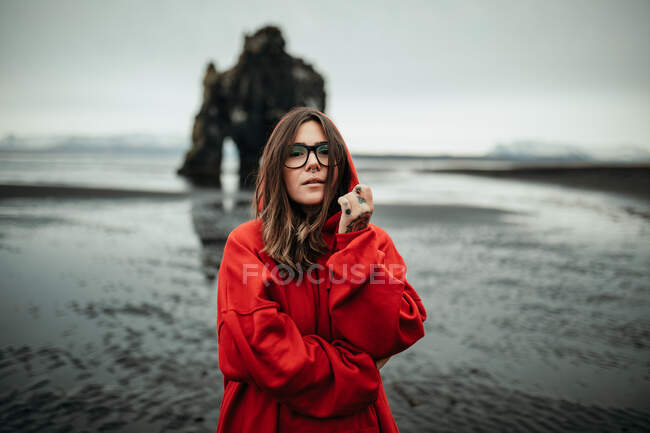 Young tourist in eyeglasses with piercing near land in water and big stone cliff on blurred background — Stock Photo
