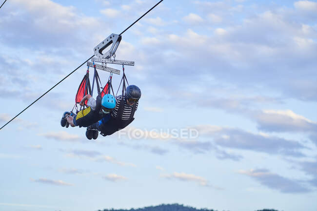 Anonymous brave people in safety equipment riding zip line over mountains in summer — Stock Photo