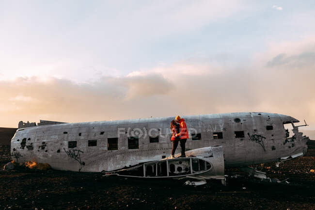 Молода пара стоїть на зруйнованому літаку між покинутими землями і блакитним небом — стокове фото