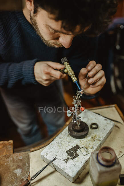 Anonymous jeweler with dirty hands using tongs to bend small metal blank while working in workshop — Stock Photo