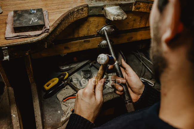 Anonymous goldsmith hammering and expanding ring blank on metal stick while working in workshop — Stock Photo