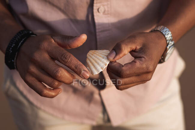 Crop anonymous black male in silver metallic wristwatch and stylish bracelet holding white seashell — Stock Photo