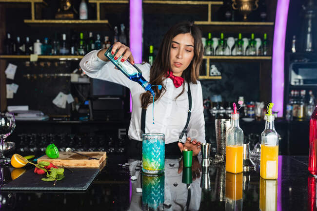 Focused female barkeeper in stylish outfit adding blue colorant liquid from  bottle into glass while preparing cocktail standing at counter in modern  bar — nightlife, elegant - Stock Photo | #508554146