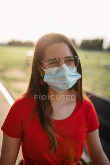Mulher encantada em máscara médica protetora desfrutando de fim de semana no parque de verão durante o coronavírus no dia ensolarado — Fotografia de Stock