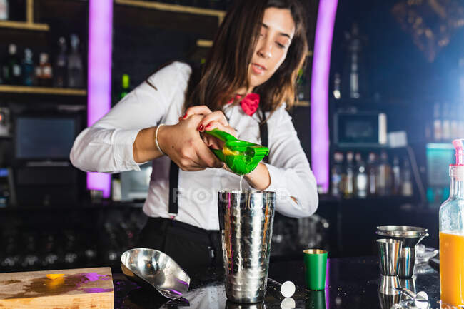 Jeune femme barman en tenue élégante serrant du citron tout en préparant un cocktail debout au comptoir dans un bar moderne — Photo de stock