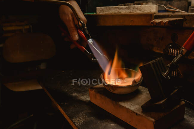 Unrecognizable goldsmith melting metal for jewellery with blowtorch while standing near workbench in workshop — Stock Photo