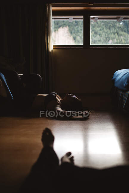 Young tattooed pensive woman in lingerie resting on ground in obscurity — Stock Photo