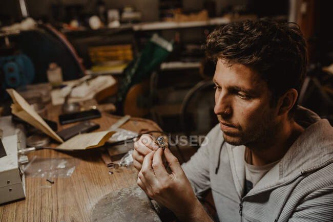 Juwelier hält unfertigen Ring in schmutzigen Händen und überprüft Qualität in Werkstatt — Stockfoto