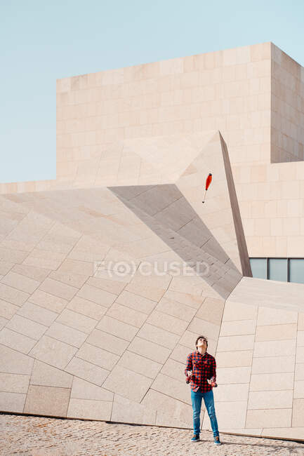 Full length of male performing trick with juggling clubs while standing against contemporary stone building with unusual geometric architecture — Stock Photo