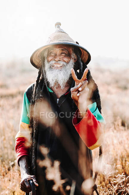 Fröhlicher alter Rastafari mit Dreadlocks, der auf einer trockenen Wiese in der Natur in die Kamera blickt — Stockfoto