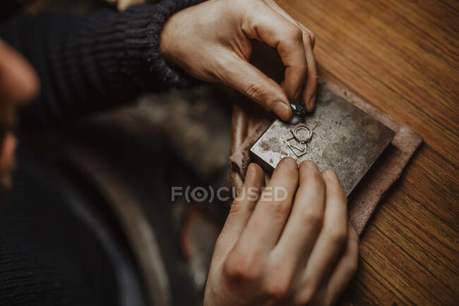 Unbekannter Goldschmied hält Edelstein und Metallschmuck über Tisch, während er in Werkstatt Ring herstellt — Stockfoto