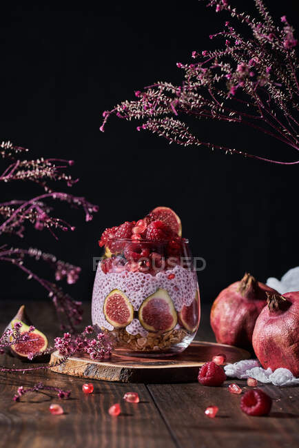 Vista lateral de mermelada de fruta fresca en frasco pequeño con higos completos y cortados en el plato en la mesa de cocina negra junto a las granadas - foto de stock