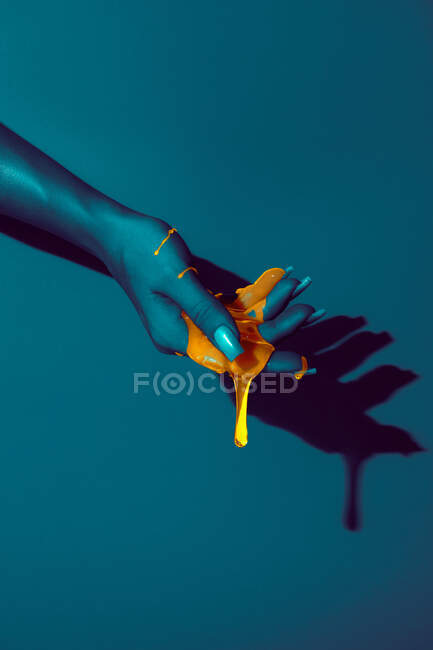 Crop unrecognizable woman showing hand with manicure and bright paint fluids in ultraviolet light on blue background — Stock Photo
