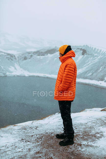 Side view of young tourist on peak of mountain in snow looking at water in valley — Stock Photo