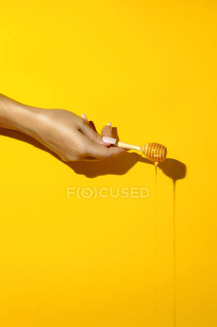 Crop femelle anonyme avec manucure démontrant trempette avec du liquide de miel savoureux sur fond jaune vif — Photo de stock