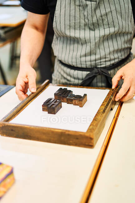 Recorte maestro masculino irreconocible que trabaja con letras de metal de tipografía en marco de madera mientras está de pie en la mesa en tipografía - foto de stock