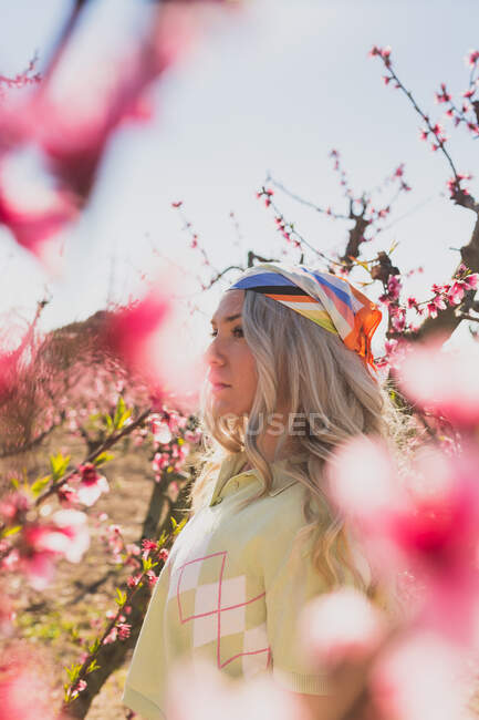 Female surrounded by fresh flowers growing on tree branches in garden looking away — Stock Photo