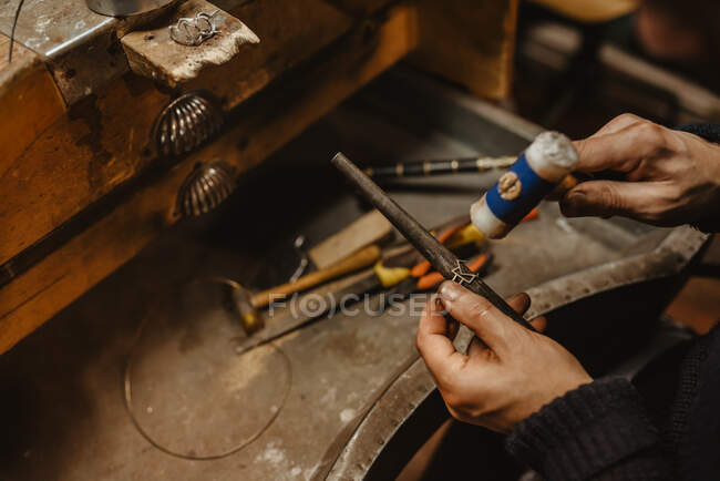 Anonyme orfèvre martelant et élargissant anneau blanc sur bâton de métal tout en travaillant dans l'atelier — Photo de stock