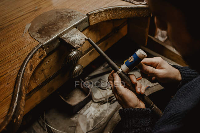 Anonymous goldsmith hammering and expanding ring blank on metal stick while working in workshop — Stock Photo