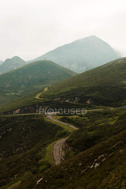 Thick gray clouds floating on sky over green hills and sinuous road on dull day in countryside — Stock Photo