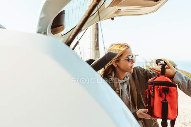 Mulheres em casacos colocando sacos no porta-malas do carro se preparando para a viagem de carro juntos — Fotografia de Stock