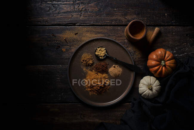 Top view of various ground handfuls of pumpkin spices on dishware and spoon at wooden plank table — Stock Photo